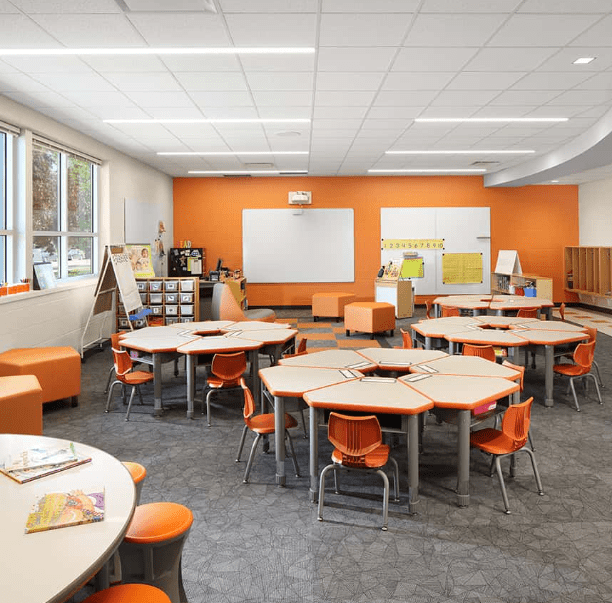 A classroom with orange chairs and tables.