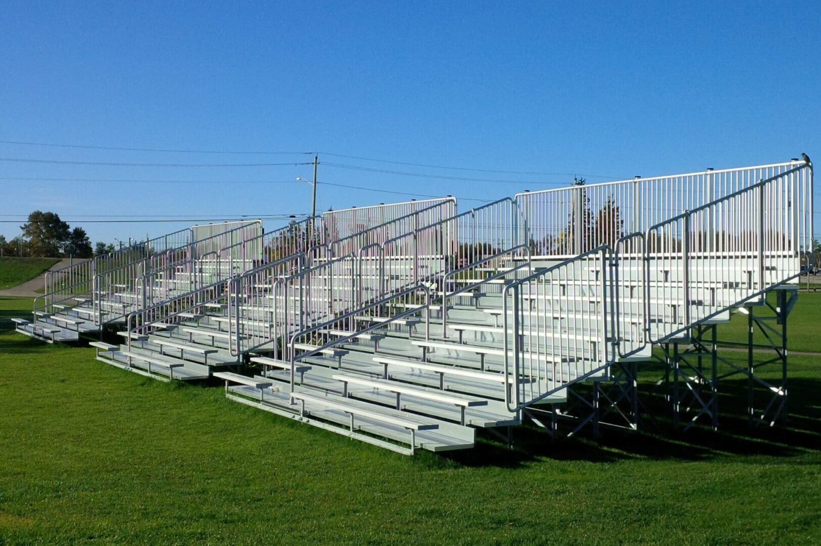 A bleacher with metal rails and seats in the middle of an empty field.