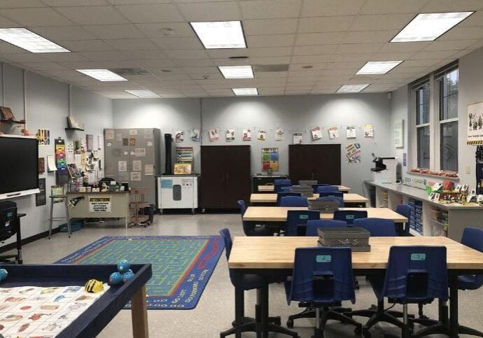 A classroom with tables and chairs, desks and rugs.