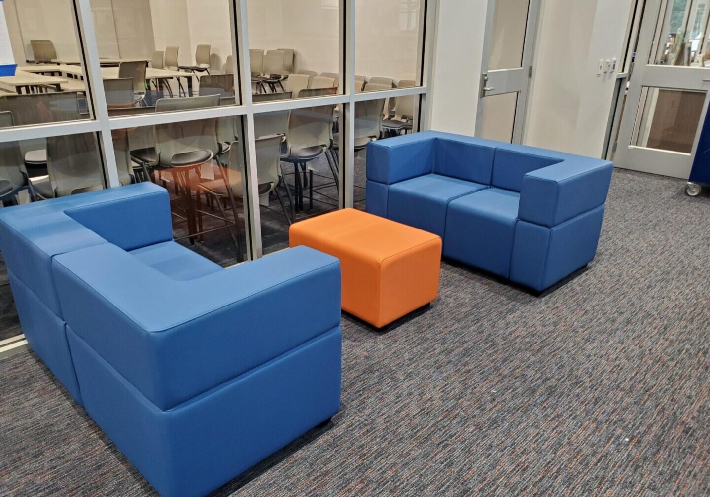 A room with two blue couches and an orange ottoman.